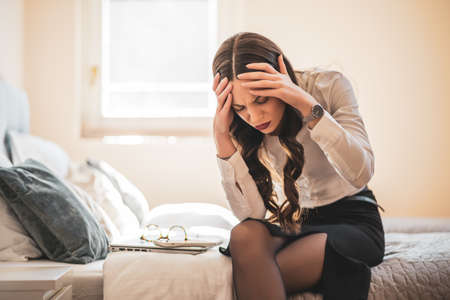 Tired businesswoman on business trip sitting in hotel room with headache.の写真素材