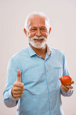 Portrait of cheerful senior man who is holding apple and smiling.の写真素材