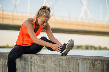 Young woman is having pain in her ankle while exercising and jogging outdoor.