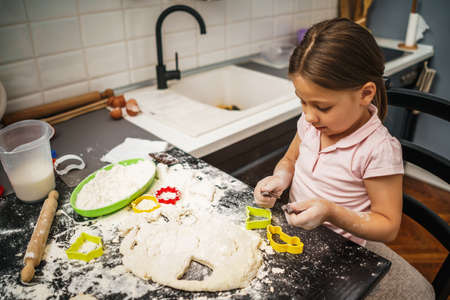 Little is plating with dough, she is making cookies in kitchen.