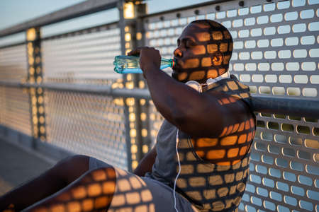 Portrait of young cheerful african-american man in sports clothing who is drinking water after jogging.の写真素材