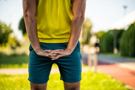 Young man is exercising outdoor. He is stretching his body and warming up for jogging.