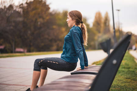 Beautiful adult woman is exercising outdoor on cloudy day in autumn. She is doing reverse push-ups.の写真素材