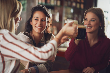 Three happy girlfriends are having fun time in pub. They are drinking beer. Friendship concept.の写真素材