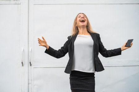 Outdoor portrait of ecstatic businesswoman who is holding smartphone.の写真素材