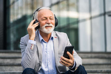 Happy senior businessman is relaxing after work in front of company building.の写真素材