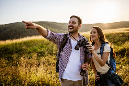 Happy couple is hiking in mountain. They are watching nature with binoculars.の写真素材