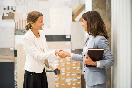 Businesswoman owning small business tiles store. She is handshaking with a satisfied customer.の写真素材