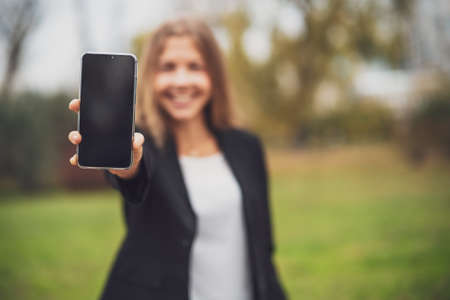 Outdoor portrait of happy businesswoman who is holding smartphone with blank screen.の写真素材
