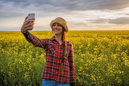 Proud female farmer is taking selfie in front of her rapeseed field.の写真素材