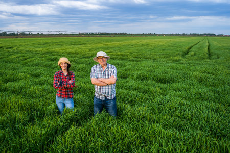 Proud two generations farmers are standing in their barley field in sunset.の写真素材