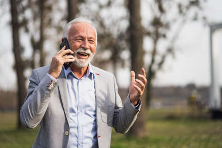 Happy senior businessman is relaxing after work. He is talking on smartphone.の写真素材