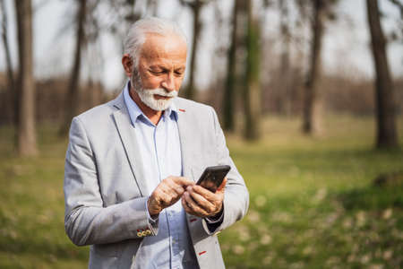 Happy senior businessman is relaxing after work. He is messaging on smartphone.の写真素材