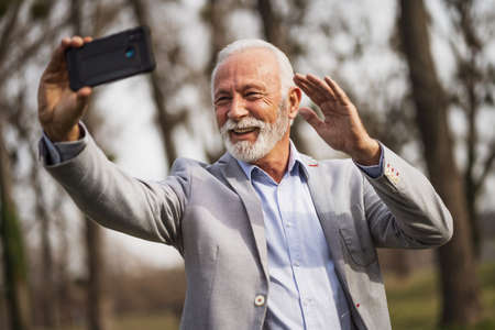 Happy senior businessman is relaxing after work. He is messaging on smartphone.