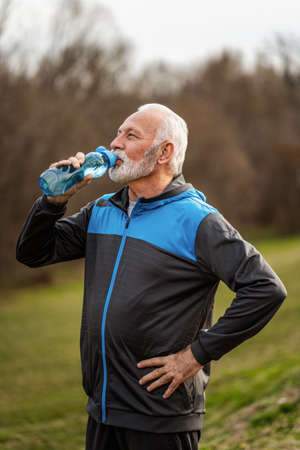 Senior man is drinking water after exercising in park.