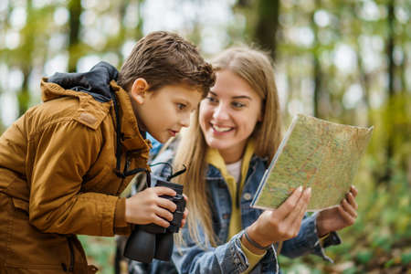 Happy mother and son are hiking in forest. Boy is watching nature with binoculars.の写真素材