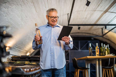 Portrait of senior man who owns winery. He is examining quality in his wine cellar. Industry wine...