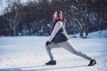 Adult man is exercising in park in wintertime. He is stretching his body before jogging.の写真素材