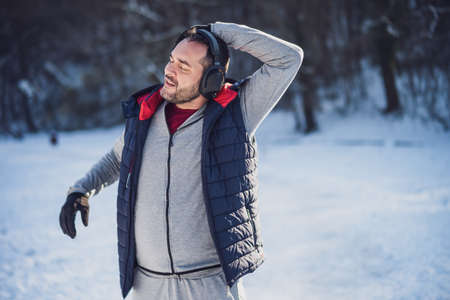 Adult man is exercising in park in wintertime. He is stretching his body before jogging.