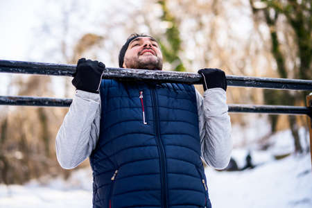 Adult man is exercising on pull-up bar in park in wintertime.の写真素材