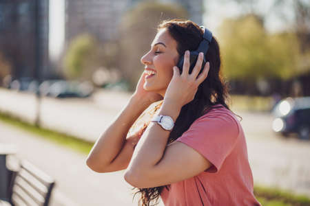 Happy young woman is enjoying sunny day outdoor in city. She is listening music on headphones.の写真素材