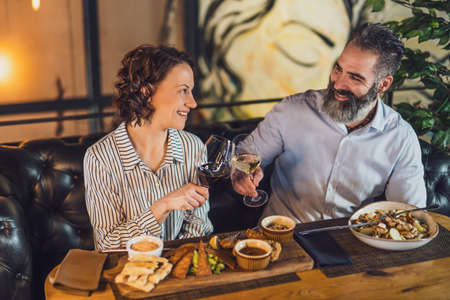 Happy couple is sitting at restaurant. They are having dinner with wine and spending nice time together.の写真素材