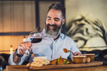 Happy adult man is having dinner and wine at restaurant.