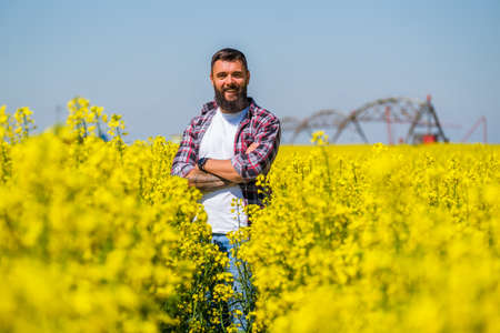 Portrait of happy and successful farmer who is standing in his rapeseed field. Rapeseed plantation in bloom.の写真素材