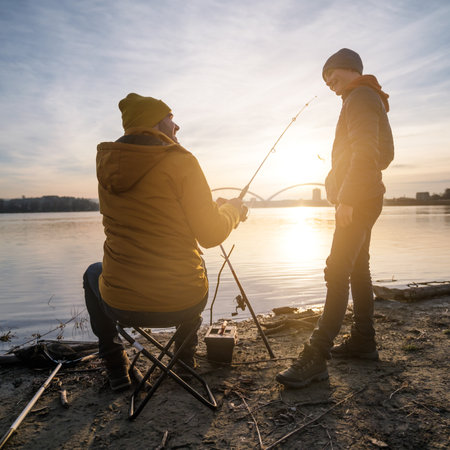Father and son are fishing on winter day. River fishing. Teenage boy is learning to fish.の写真素材