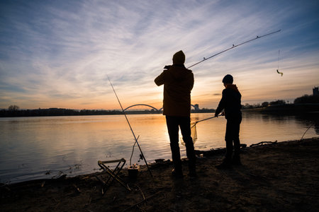 Silhouette of father and son fishing on the river at sunsetの写真素材