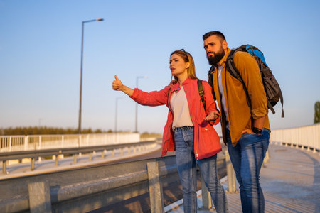 Adult couple hitchhiking on roadside trying to stop car. They are anxious and bored.の写真素材