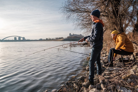 Father and son are fishing on sunny winter day. Freshwater fishing. Teenage boy is learning to fish.の写真素材