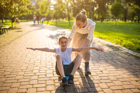 Mother having fun with her son in park on sunny day. Boy is ridding skateboard and his mother is pushing him.の写真素材