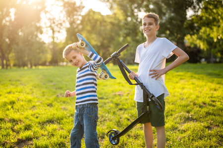 Two boys are having fun with skateboard and scooter in park. Playful children in park, happy childhood.の写真素材