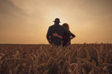 Man and woman are standing in their agricultural field in sunset. They are cultivating wheat and enjoying good agricultural season.の写真素材