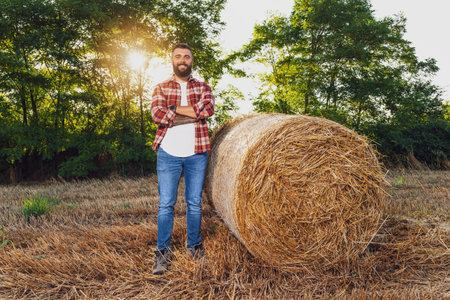 Farmer is standing beside bales of hay. He is satisfied after successful harvesting.の写真素材