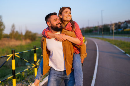 Happy smiling couple enjoying sunset. Man is carrying on back his woman.の写真素材