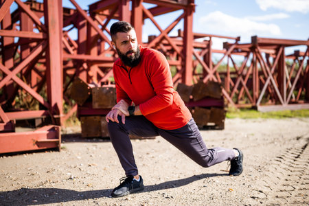 Adult man is exercising outdoor on sunny day. He is stretching his body.