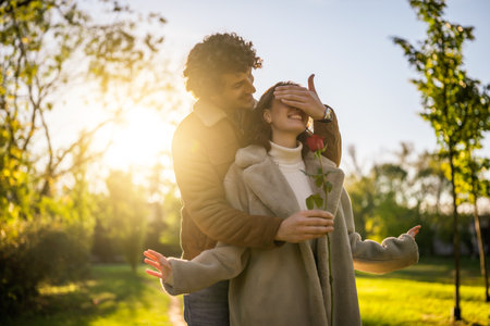 Portrait of happy loving couple in park in sunset. Man is giving rose to his woman.の写真素材