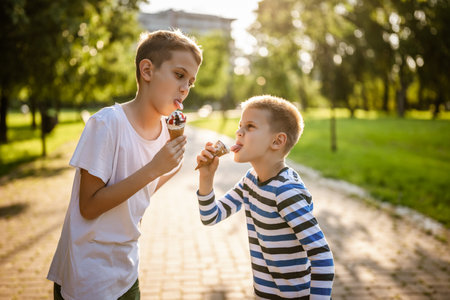 Two brothers are eating ice cream in park in summer. They are having fun and mocking at each other.の写真素材