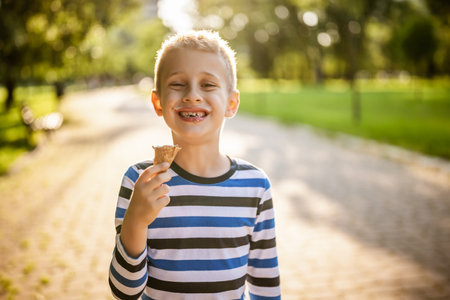 Portrait of happy boy who is standing in park and eating ice cream.の写真素材