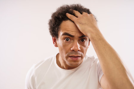 Handsome mixed race adult man is looking at wrinkles at his forehead.の写真素材