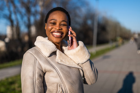 Outdoor portrait of happy black woman. She is talking on phone.の写真素材