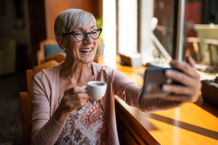 Mature woman is sitting in cafe and relaxing. She is using smartphone.