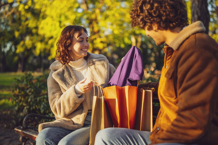 Couple sitting on bench in park. Woman is showing clothes to her man after shopping.の写真素材