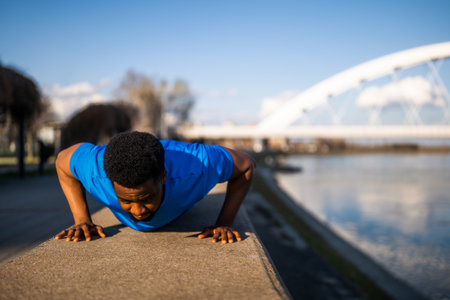 Young african-american man is exercising in the city. He is doing push-ups.