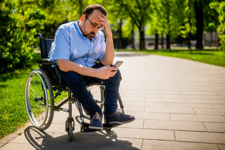 Disabled man in a wheelchair using a mobile phone in the parkの写真素材
