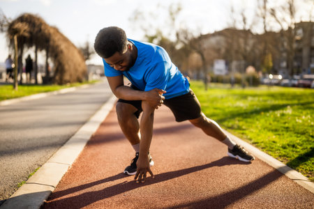 Young african american man in blue t-shirt and shorts warming up before jogging in the parkの写真素材