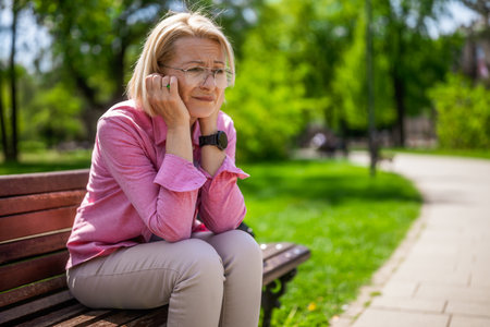 Senior woman sitting on a bench in the park and looking at the cameraの写真素材