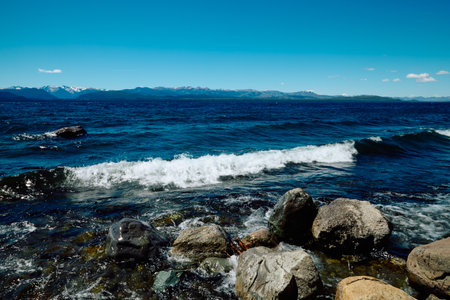 rocky shore of a blue lake, on the horizon a landscape of mountains with peaks covered with snow, Bariloche National Parkの写真素材